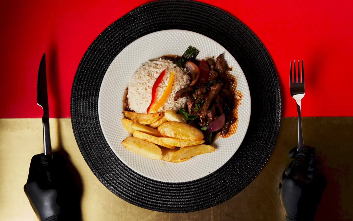 Lomo saltado con arroz y papas fritas servido sobre mantel rojo